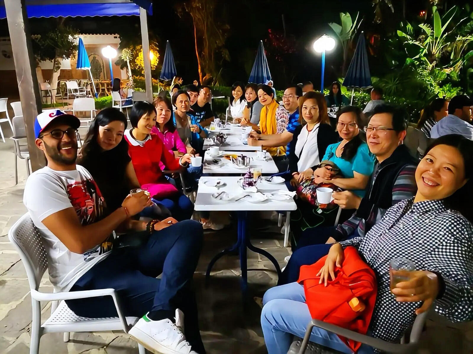 Solving Real Challenges with Happy Chinese Tour Groups Reda Akrime casually dressed with 14 Chinese tourists smiling at a night cafe in Morocco, taking a group photo