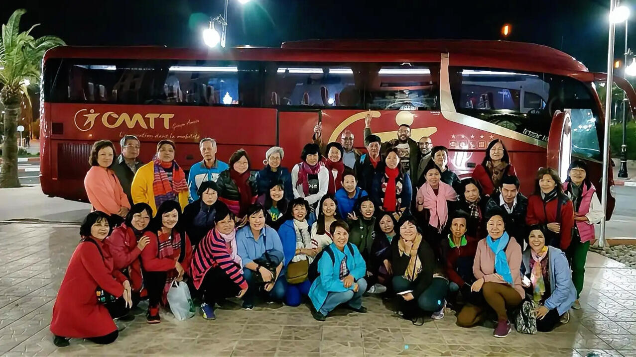 Managing Large Chinese Tour Groups on the Ground in Morocco Reda Akrime with 40 Chinese tourists taking a group photo in front of a tour bus in Morocco